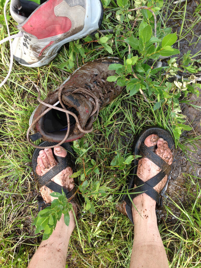 Me wearing Chaco sandals next to my mud-covered hiking boot.