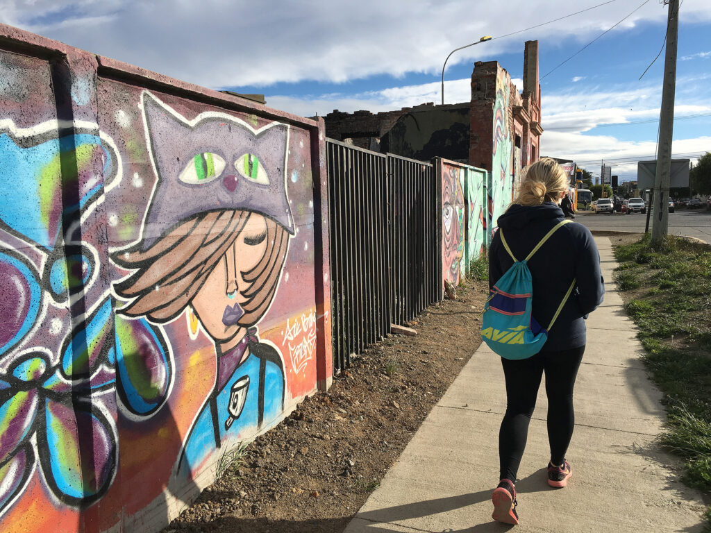 Mary Kate walking by a painted mural of a girl wearing a cat hat.